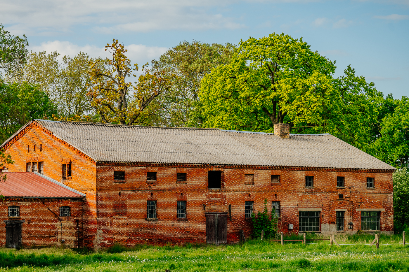 Großes historisches Backstein-Wirtschaftsgebäude mit alten Bäumen in Holzendorf.