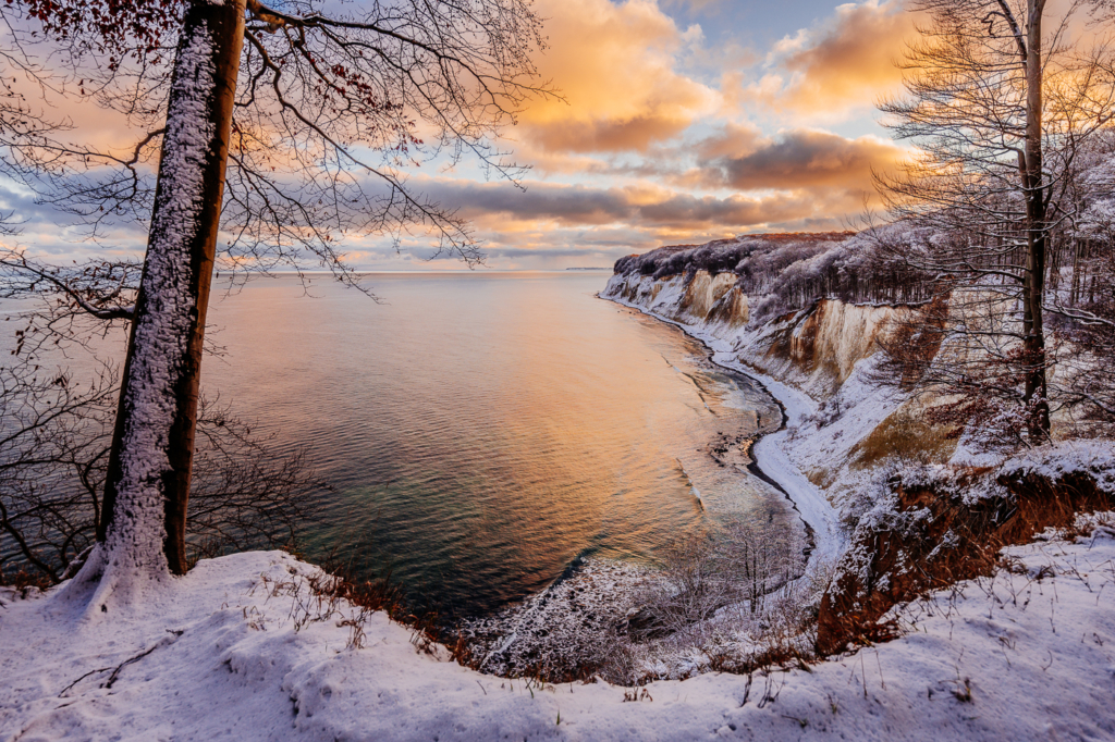 Winterliche Kreideküste im Nationalpark Jasmund auf Rügen mit Schnee, Ostsee und warmem Licht am Himmel.