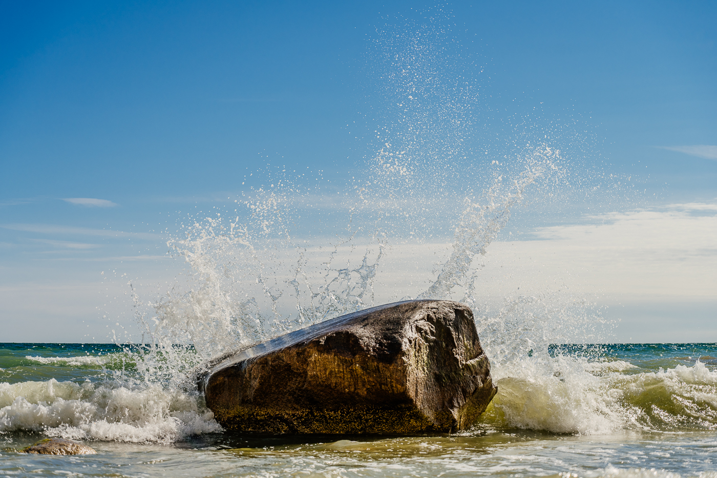 Eine Ostseewelle bricht mit hoher Gischt an einem großen Findling vor der Kreideküste des Nationalparks Jasmund.