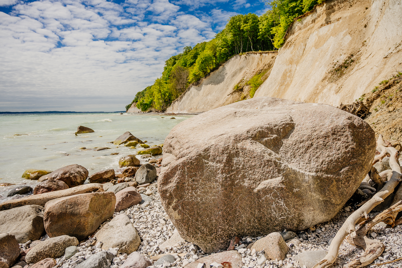 Gewaltiger Findling am Strand vor den Kreidefelsen und dem frühlingsgrünen Buchenwald des Nationalparks Jasmund auf Rügen.