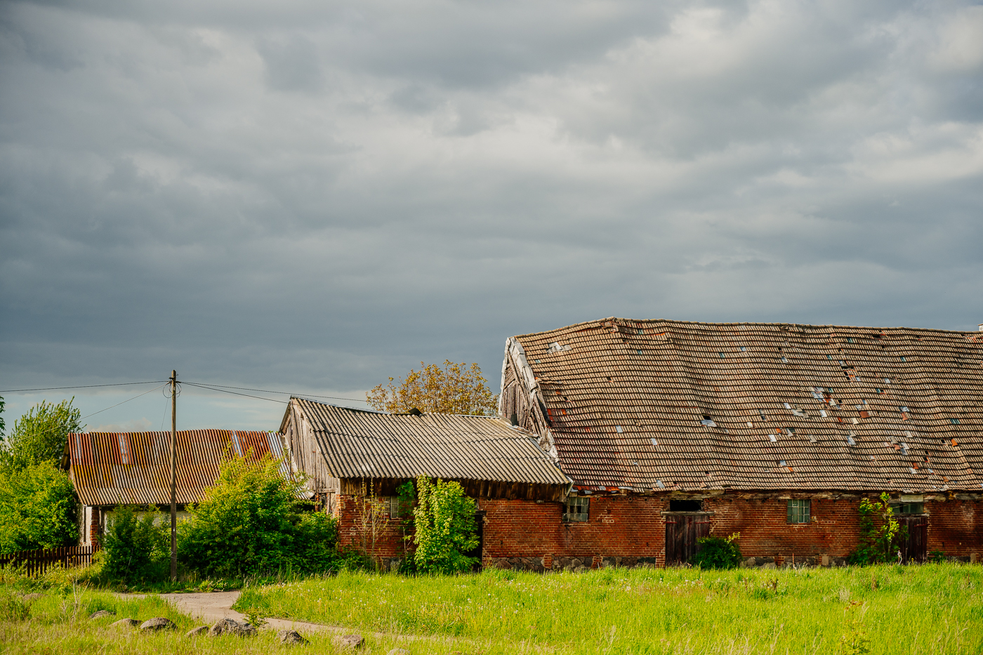 Alte Backsteinscheune und Wirtschaftsgebäude in Rittgarten unter dunklem Wolkenhimmel.