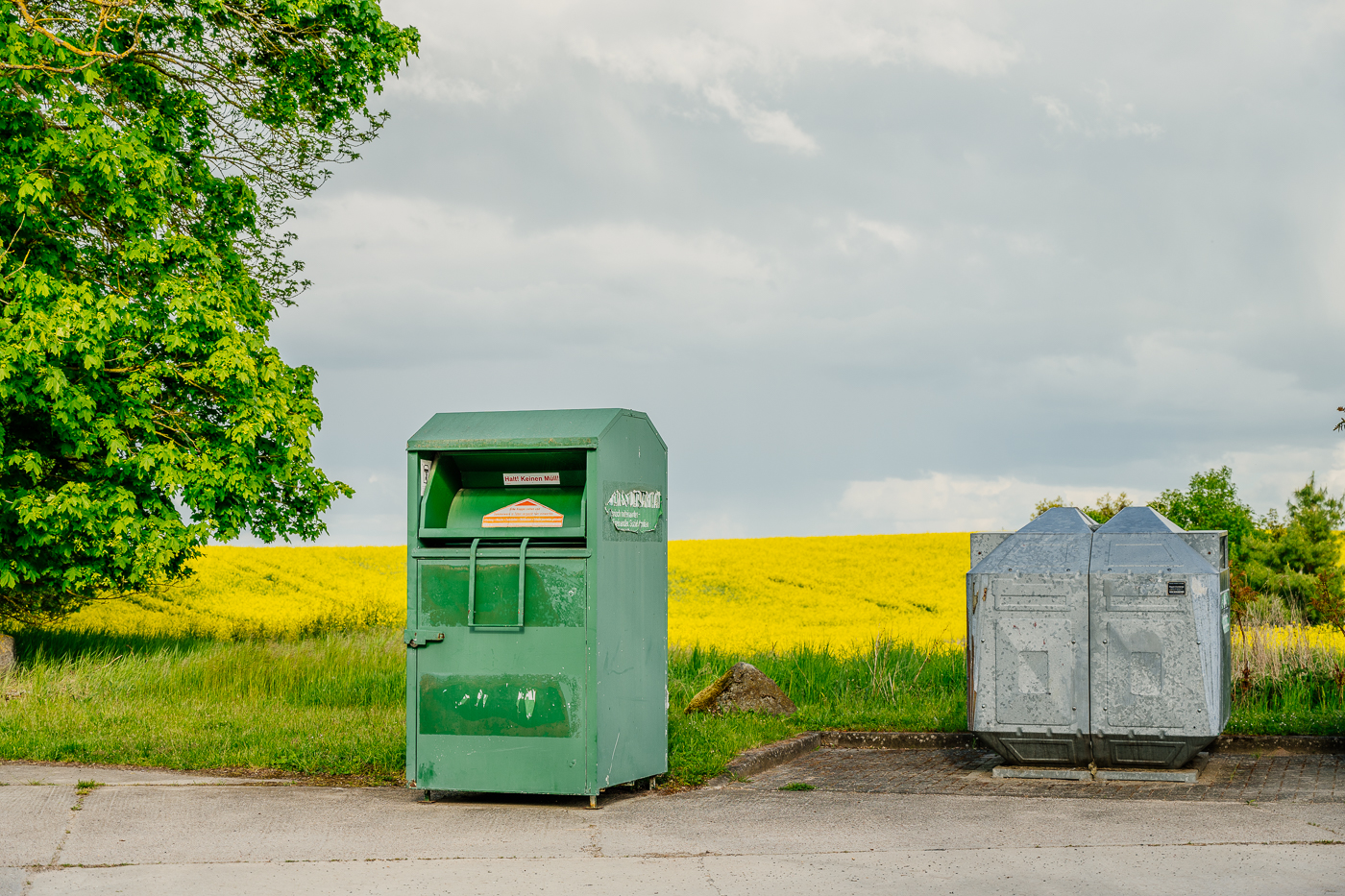 Altkleider- und Müllcontainer vor einem leuchtend gelben Rapsfeld in Rittgarten.