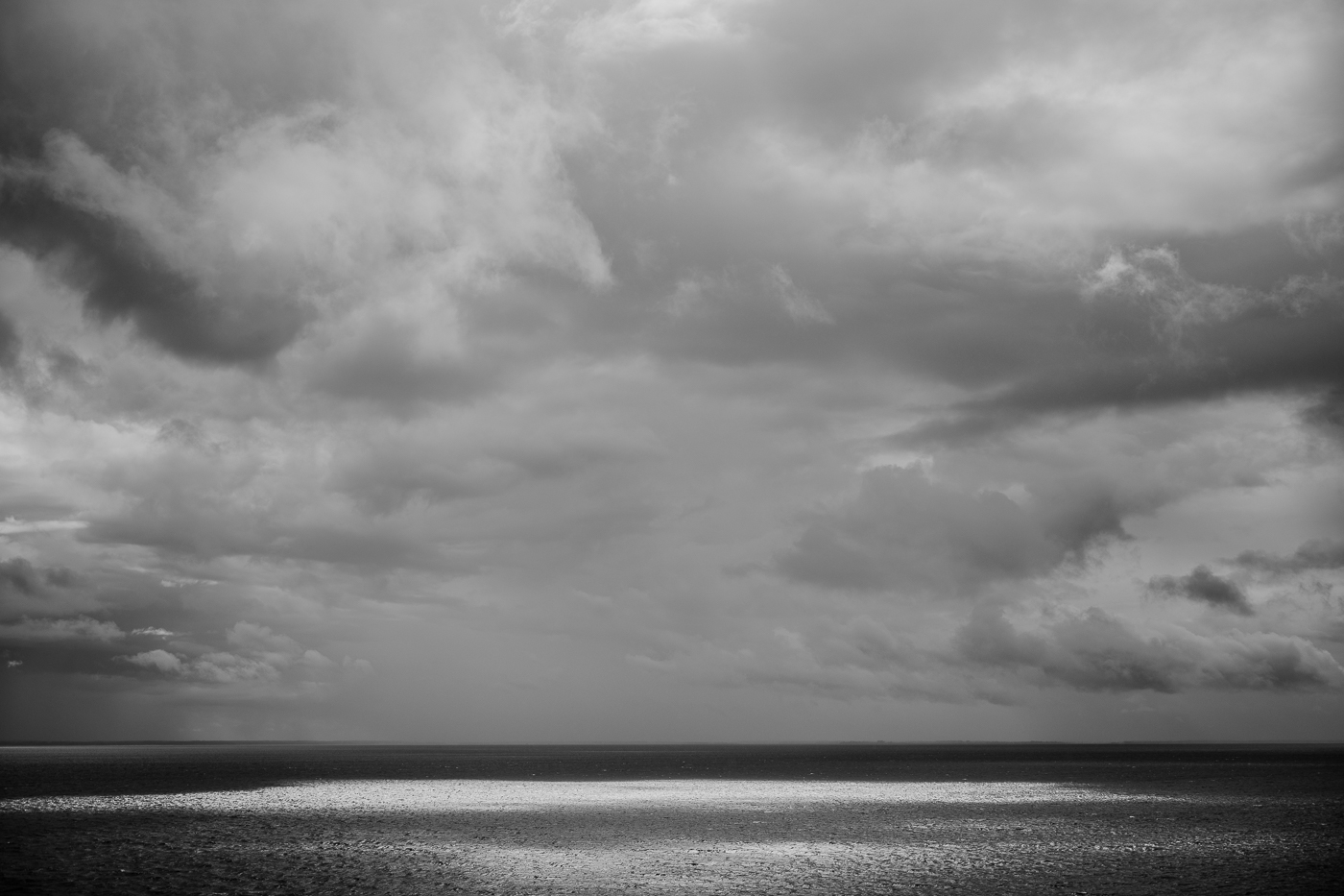 Regenwolken über dem Greifswalder Bodden bei Groß Zicker mit Sonnenlicht auf dem Wasser.