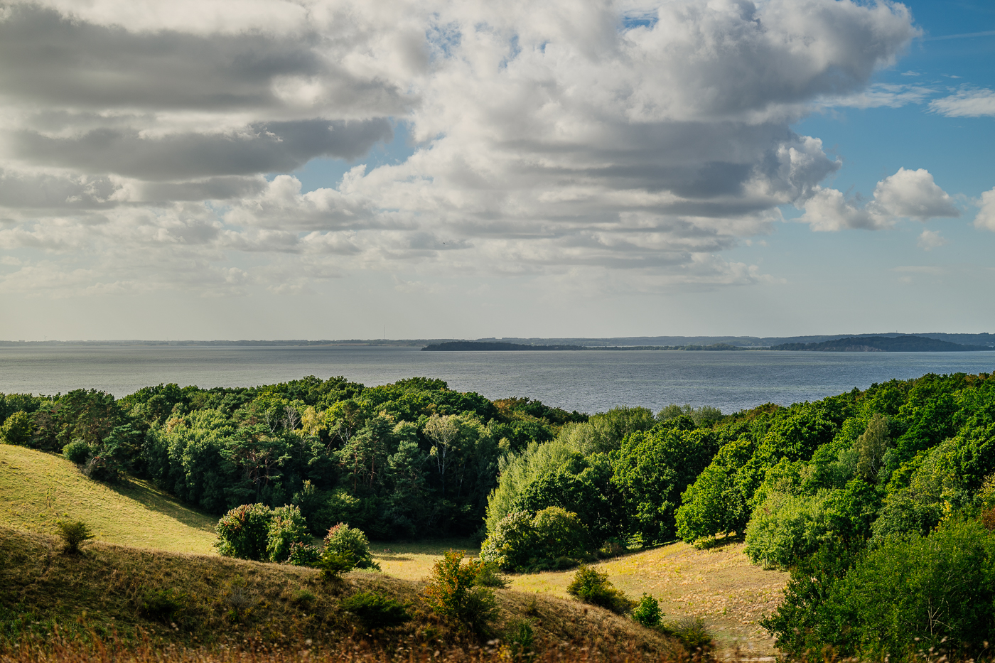 Spätsommerliche Hügel und Wälder der Zickerschen Berge mit weitem Blick über den Greifswalder Bodden unter wechselnden Wolken.